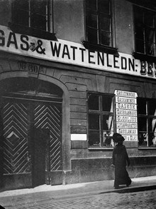 En kvinna passerar porten vid Högbergsgatan 30 A. Firman Beskow & Co, gas och vattenledningar, har skyltar på fasaden