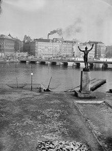 Strömparterren med utsikt mot Strömbron. I förgrunden fiskehåvar och Milles staty ""Solsångaren"". I fonden syns Grand Hotel med byggnadsställningar