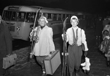 Resenärer vid långfärdsbussar dagen före julafton. Två kvinnor med bagage och vintersportutrustning