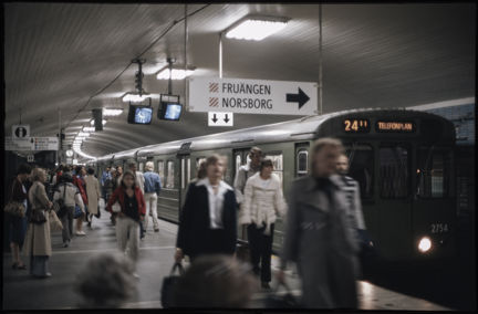 Ett myller av folk på perrongen vid T-Centralen. Ett tåg mot linje 24 mot Telefonplan har stannat till vid perrongen. 