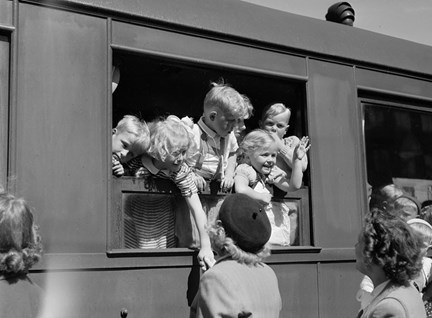 Barn står i ett tågfönster, ett av dem sträcker sig ut och håller en kvinna, sin mamma?, i handen. 