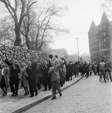 Fredsdagen den 7:e maj 1945. 
Glada flaggviftande folkmassor längs Strandvägens östra del. 
Till vänster vedtravar längs gatan.