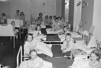 Barn ligger skavfötters i sjukhussängar i en sovsal.