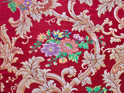 Ett rött sidentyg med motiv av blommor och rankor. I mitten finns ett motiv av färglada blommor.