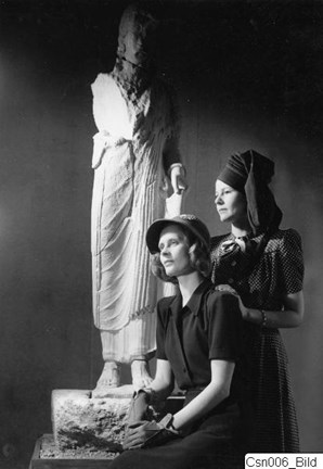 Två kvinnor, fotomodeller, fotograferade i toppmoderna hattar intill en av de cypriotiska skulpturerna i utställningen "Före Fidias" 1941.