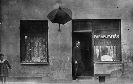 En man står på trappen till entrén till en paraplyaffär. Från fasaden sticker det ut en skylt som föreställer ett paraply. 