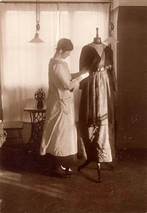 Foto på kvinna som ändrar en klänning på en provdocka. I bakgrunden en symaskin.