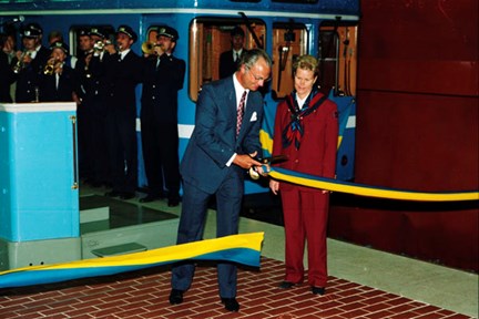 Kung Carl XVI Gustaf klipper ett blågult band på en tunnelbaneperrong. Ett tunnelbanetåg och en blåsorkester i bakgrunden.