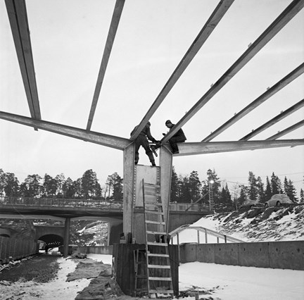 Två män på en konstruktion som ska hålla uppe ett tak.