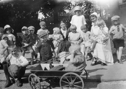 Gruppbild av barn och barnsköterskor i trädgården till Kungsholmens västra barnkrubba.