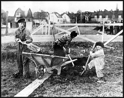 en familj, pappa, mamma, barn gräver på sin tomt och lägger jorden i en skottkärra inför grundläggning av deras hus.