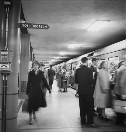 Kvinna går på perrong under en skylt med texten "Mot Förorten". 