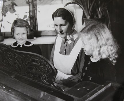 Svartvitt fotografi med föreståndaren på Kungsholms barnkrubba samt två flickor på varsin sida om henne. 