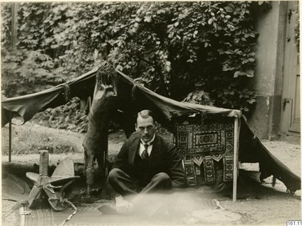 Svartvitt fotografi av en en man i västerländska kläder, som sitter med korslagda ben i ett tält.