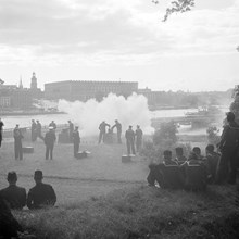 Flottister skjuter med små kanoner på Skeppsholmen. Stockholms slott i bakgrunden