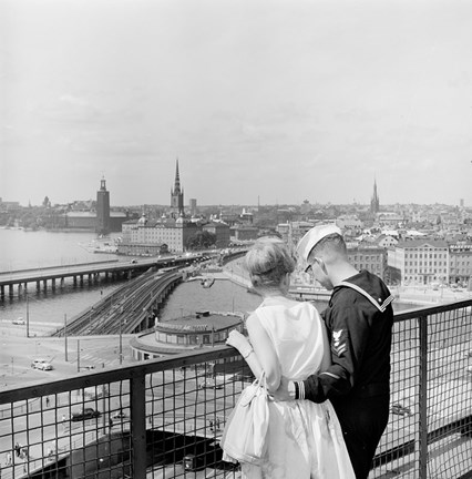 Ung kvinna i ljus klänning, ung man i sjömanskostym, sedda bakifrån.