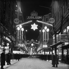 Julskyltning längs Drottninggatan söderut vid korsningen Kungsgatan med varuhuset PUB. Skyltningen är tillägnad  firandet av Drottninggatans 300-års jubileum, 1637 - 1937.