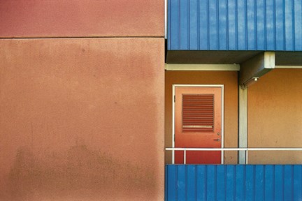 Fasad i gulbrunt med blå balkonger och en röd dörr