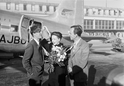 Utanför ett mindre flygplan står tre personer. En man vars lugg blåser i pannan på honom. En kvinna, skådespelerska, med en blombukett i famnen som håller hårt i hatten så att den inte ska blåsa av. Längst till höger står regissören Ingemar Bergman.
