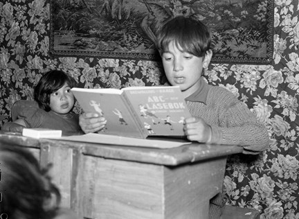 Interiörbild med läsande pojke i en skolbänk i den första skolan för romer som just öppnats i familjen Taikons tält vid romernas läger vid Lilla Sköndal i Gubbängen.