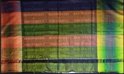 Skimrande vävda röda och rostgröna färgfält, vävd text.