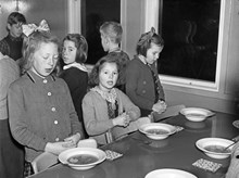 Barn vid matbord i skolbespisning står upp med knäppta händer och läser bordsbön.