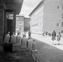 Gubbängens folkskolas skolgård med femtioliters mjölkkannor utanför skolbespisningen.