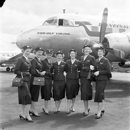 Sju leende flygvärdinnor i uniform står uppradade framför ett SAS-plan med namnet "Torolf Viking" på nosen. 