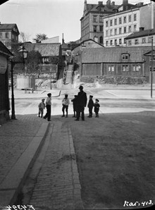 En man och några barn står vid Erstagatan 14. Erstagatan och Erstagatans trappor norrut vid korsningen med Folkungagatan