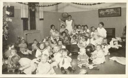 Svartvit bild av barnen på Lilla Hemmet samlade framför julgranen med sina vårdare.