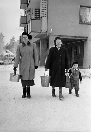 Två kvinnor i kappa och mössa med varsin hink. Pojke i overall. Snö.