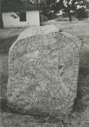 Kistastenen i svartvitt. I bakgrunden ses Kistagård och en liten landsväg.