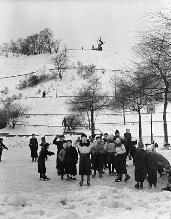 Nedanför en hög kulle syns en mindre isbana. Ett tjugotal barn, främst pojkar, åker skridskor på isen eller står stilla och poserar glatt inför fotografen. 