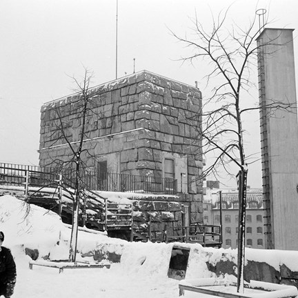 Ett torn i sten och en skorsten, första delen av uppförandet av Stadsarkivet. Nyplanterade träd i förgrunden, det är vinter.