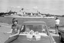 Reportage kring Kungabröllopet den 19 juni 1976. En pojke säljer nyckelringar med kungen och Silvias porträtt på Skeppsbrokajen. I bakgrunden ett militärfartyg på Strömmen